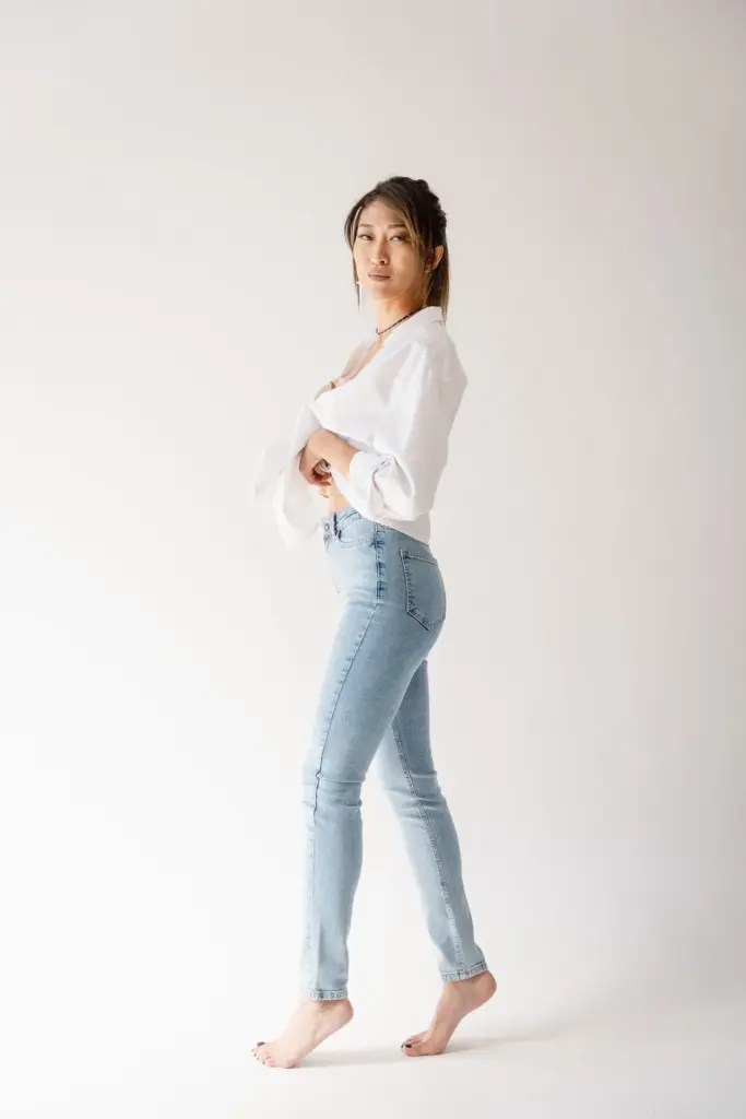 Woman wearing light blue slim-leg jeans and a white blouse against a pale studio background.