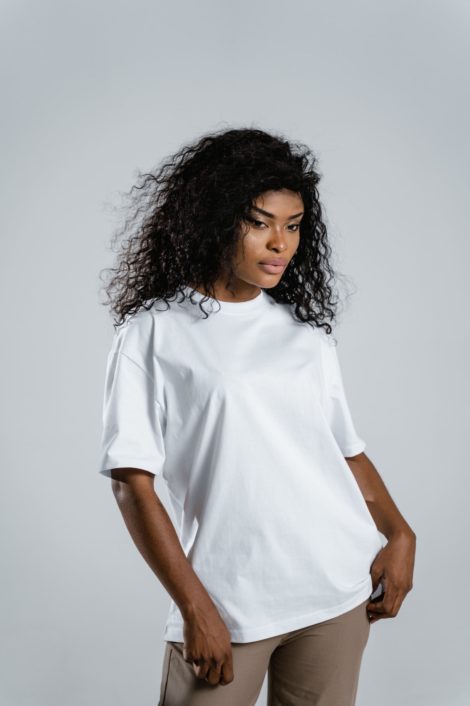 Woman wearing a plain white crew-neck T-shirt with relaxed short sleeves against a pale grey studio background.