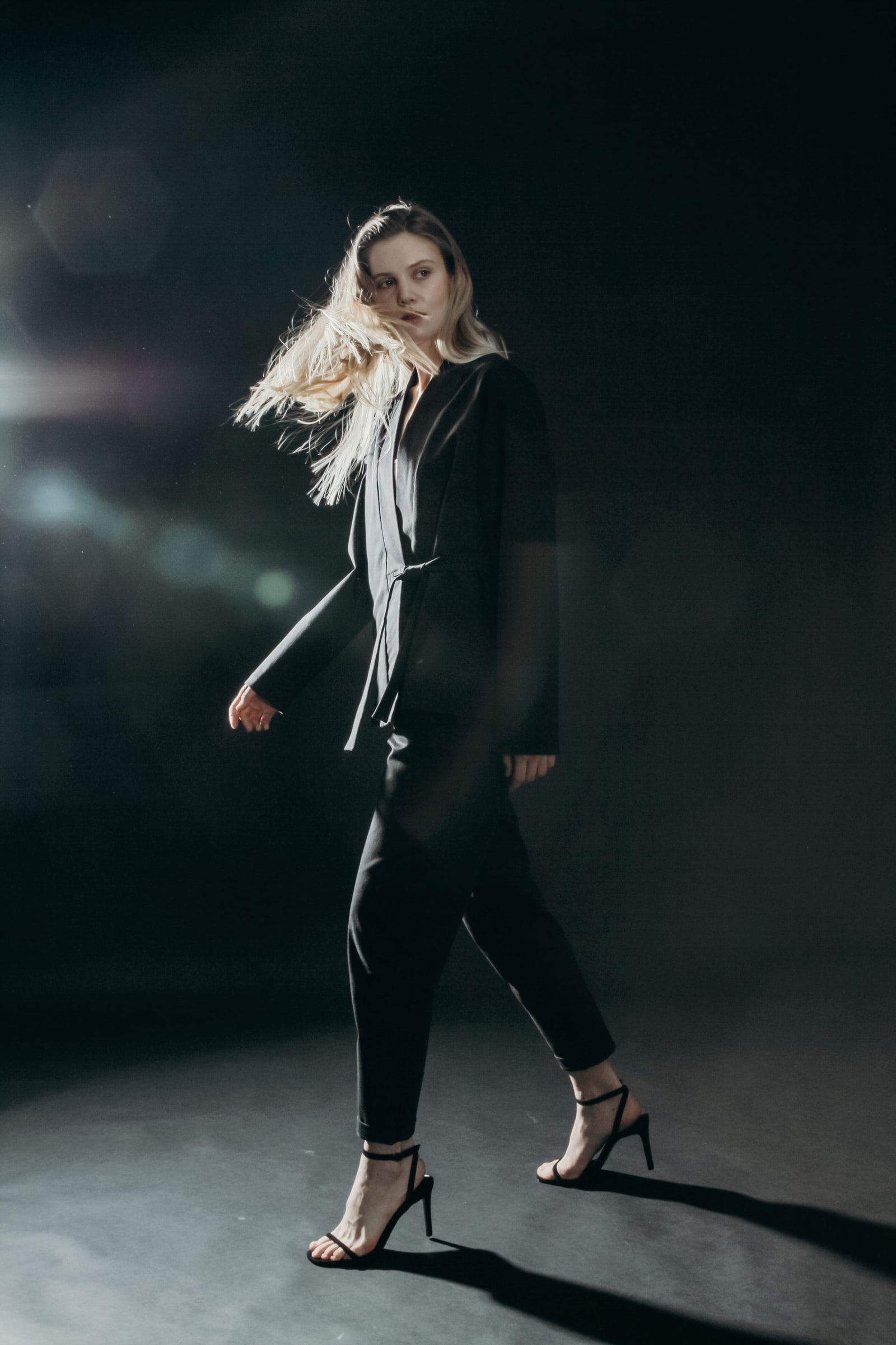 A woman wearing black tailored clothing in a dark studio.