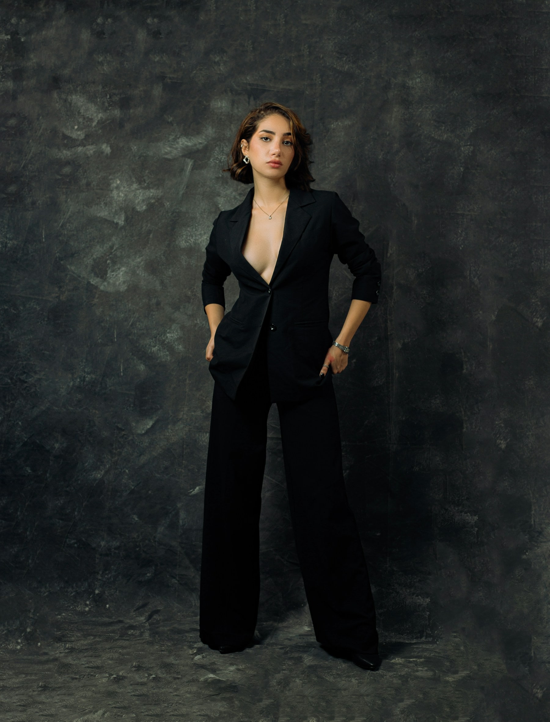 A woman in a black trouser suit against a textured dark background.