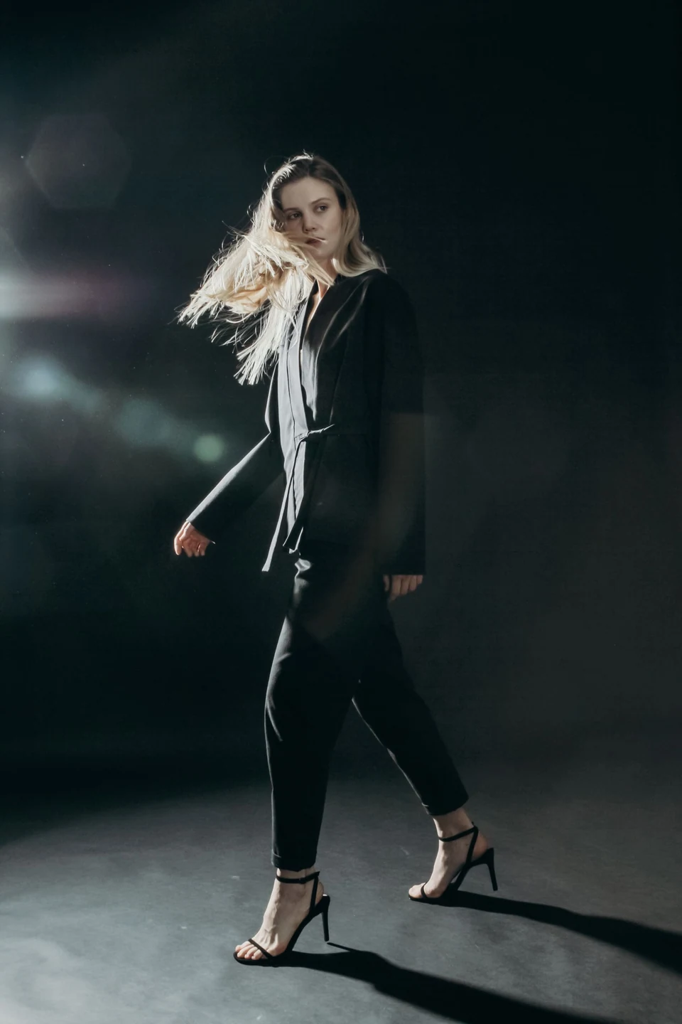 A woman wearing black tailored clothing in a dark studio.