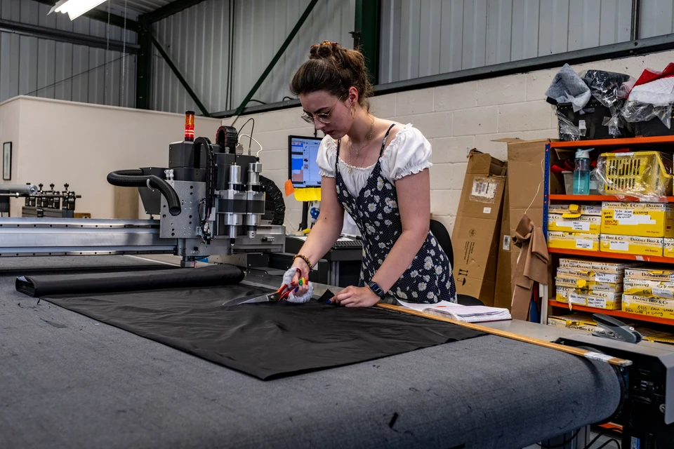 An operator preparing dark fabric on a large cutting table.