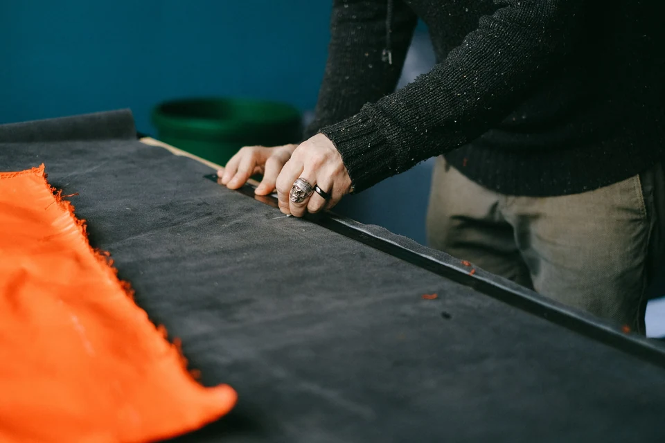 Hands checking dark fabric with a ruler.