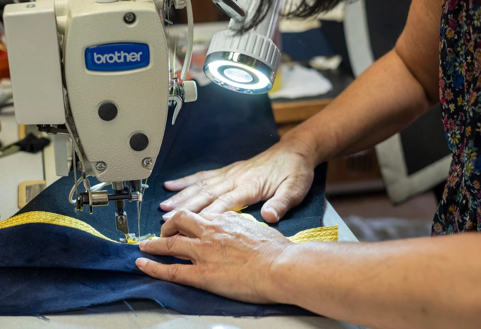 Close view of hands guiding dark fabric through a sewing machine.